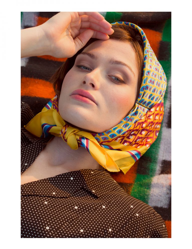 Model wearing a scarf laying down on a blanket.