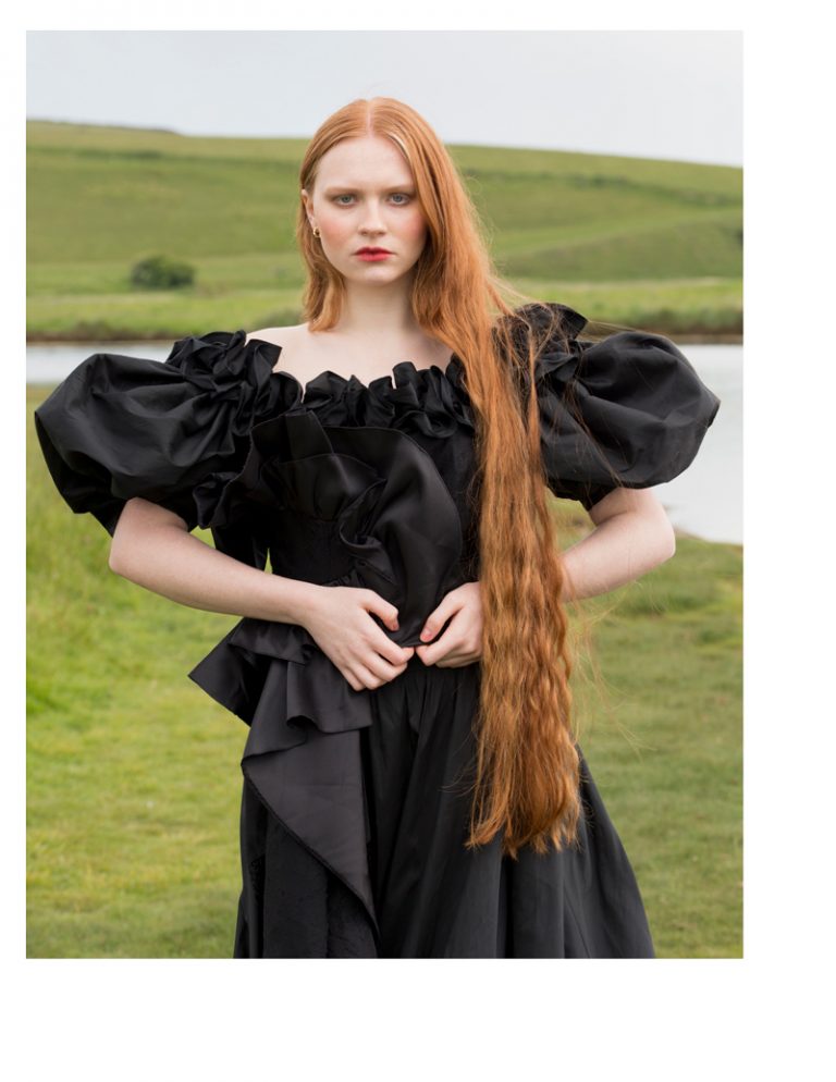 A model wearing a beautiful designer black dress by a river.