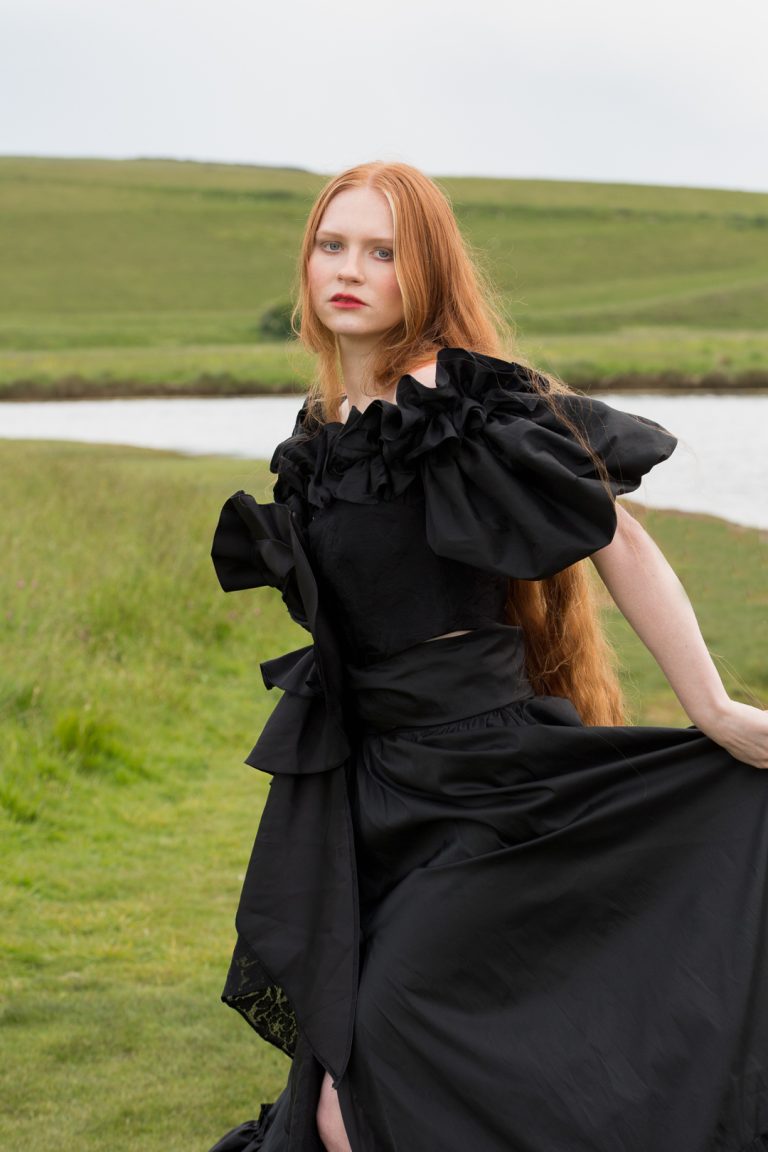 Fashion Editorial - A woman with red hair and long flowing locks wearing a black dress.