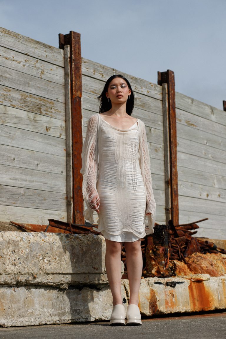 Woman in white dress standing on rock overlooking ocean.