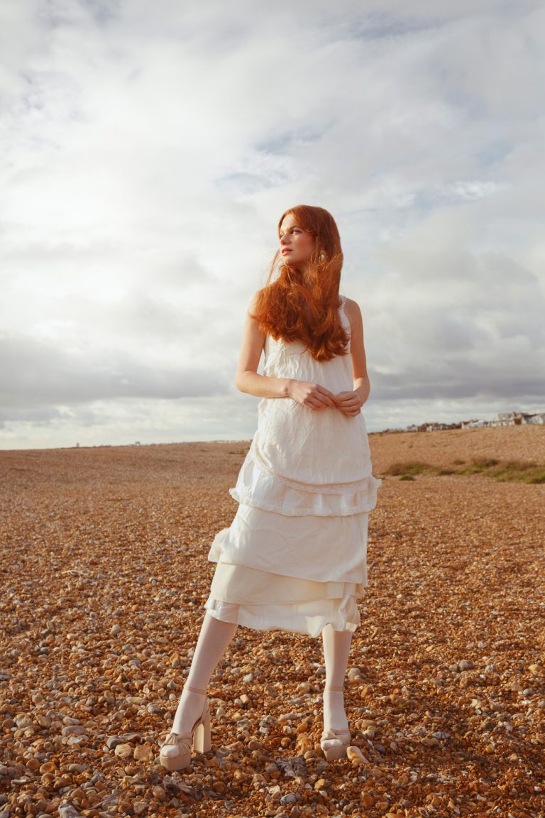 Beautiful model wearing white dress in a winter fashion shoot by Brighton seafront.